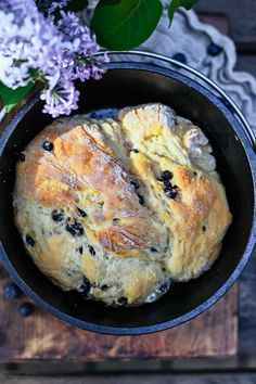 blueberry bread in a cast iron skillet on a wooden table next to lilacs