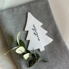 a napkin with a christmas tree on it sitting on top of a white plate next to a green plant