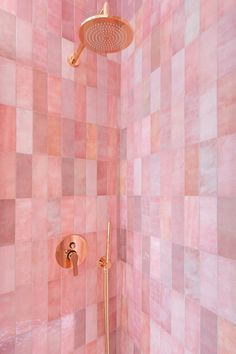 a pink tiled shower with gold faucet and hand held shower head in the corner