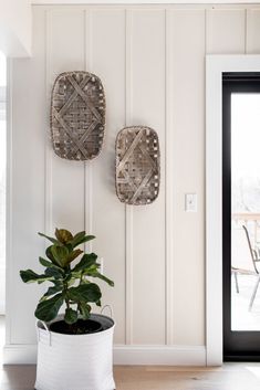 two decorative wall hangings above a potted plant in front of a white door