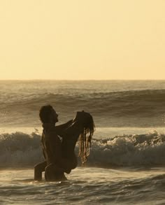 a man carrying a surfboard into the ocean at sunset with waves in the background