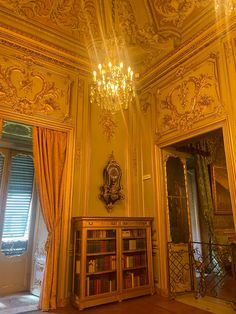 an ornate room with chandelier, bookshelf and window in the corner