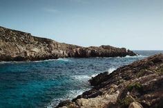 the ocean is blue and clear with waves coming in from the rocky shore on an island