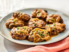 meatballs covered in sauce on a plate with a red napkin and wine glass behind it