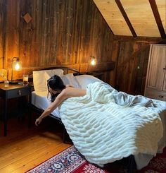 a woman laying on top of a bed in a bedroom next to a wooden wall