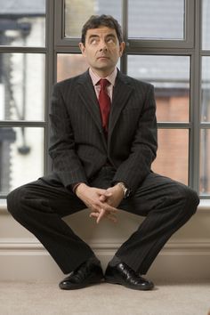 a man in a suit and tie sitting on a window sill with his hands crossed