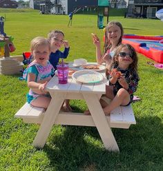 three children sitting at a picnic table eating pizza and drinking water from cups on the grass