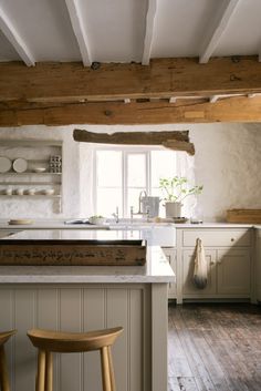 a kitchen with white cabinets and wooden beams on the ceiling, along with two stools