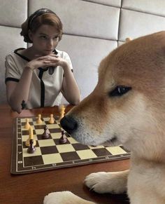 a woman sitting at a table with a dog and chess board in front of her