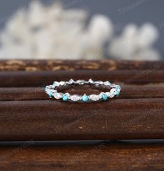 an image of a wedding ring with turquoise stones on it's side, sitting on top of a wooden table