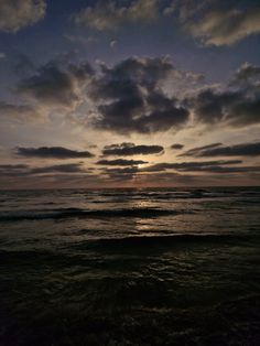 the sun is setting over the ocean with dark clouds