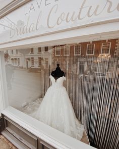 a wedding dress is displayed in the window of a bridal couture shop