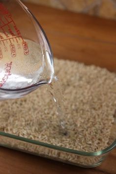 a person pouring water into a glass bowl on top of a wooden table next to a pile of carpet