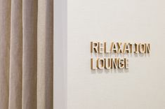 the word relaxation lounge spelled with wooden letters on a white wall next to drapes