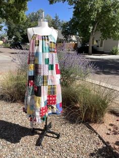 a dress made out of patchwork fabric sitting on top of a stand in front of some bushes