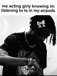 a man with dreadlocks is looking down at his cell phone while wearing a t - shirt that says, me acting girly knows im listening to its in my airpods