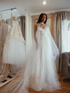 a woman is standing in front of some wedding gowns and dresses hanging on racks