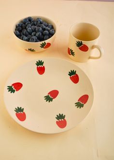 a plate with strawberries and blueberries on it next to a bowl full of berries