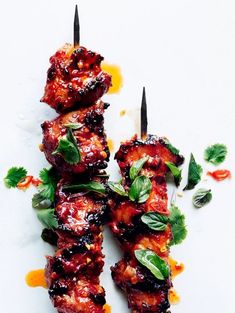 chicken skewers covered in sauce and garnished with green leaves on a white surface