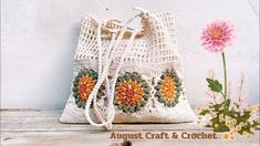 a crocheted bag sitting on top of a wooden table next to pink flowers