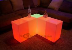 two illuminated cube tables with bottles on them in front of a couch and coffee table