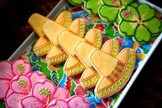 decorated cookies in the shape of surfboards and flowers on a colorful platter with green leaves