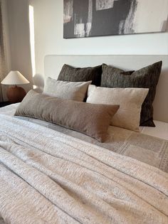 a bed with several pillows on it and a painting hanging above the headboard behind it