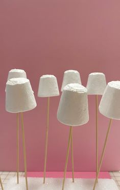 five white lamps with wooden sticks in front of a pink wall