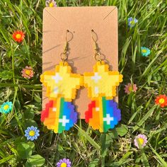 a pair of colorful pixelated earrings sitting on top of a grass covered field next to flowers