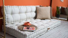 a living room with orange walls and a white couch in the middle, surrounded by pillows