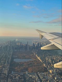 an airplane wing flying over a city with tall buildings and trees in the foreground