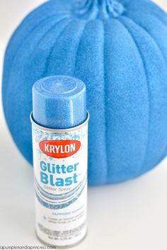 a blue pumpkin sitting next to a spray of glitter bleast on a white surface