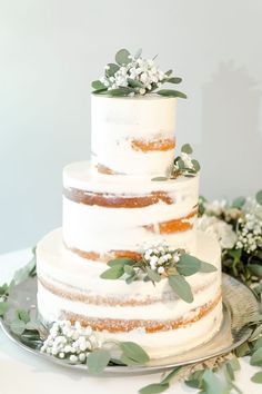 a three tiered white cake with greenery on top