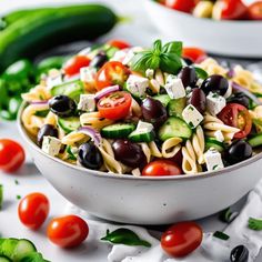 a white bowl filled with pasta salad next to cucumbers, tomatoes and other vegetables