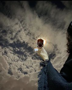 a woman holding up a donut in the sky with clouds behind her and sun shining through it