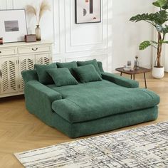 a green couch sitting on top of a wooden floor next to a white dresser and potted plant