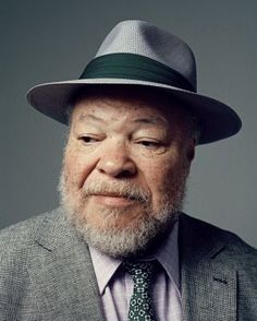 an older man wearing a gray suit and tie with a green hat on his head