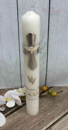 a white candle with a cross on it sitting next to some flowers and wood planks