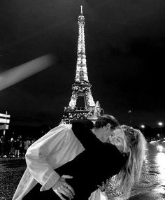 black and white photograph of couple kissing in front of the eiffel tower at night