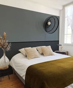 a bedroom with a bed, table and fan on the wall next to it's windows