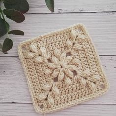 a crocheted square on a white wooden surface next to a potted plant