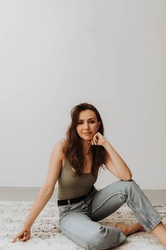 a woman is sitting on the floor in jeans and tank top with her hand under her chin