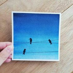 a person holding up a card with two birds sitting on wires