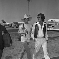 black and white photograph of man and woman walking in an airport with planes behind them