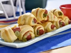 several pigs in a blanket on a plate with a red bowl and napkin behind it