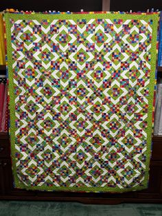 a green and white quilt hanging on a book shelf in front of bookshelves