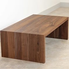 a wooden bench sitting in the middle of a room next to a white wall and floor