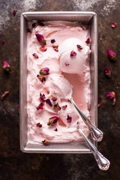 a scoop of ice cream in a metal container with pink flowers on the side and two spoons next to it