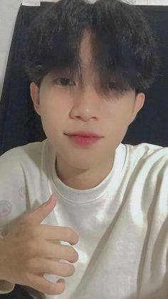 a young man with black hair is holding his hand up to the camera while wearing a white t - shirt