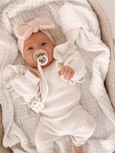 a baby is laying down with a pacifier in it's mouth and wearing a white outfit